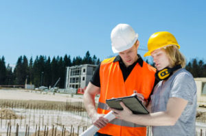 Zwei Bauarbeiter stehen auf einer Baufläche und schauen sich einen Plan an