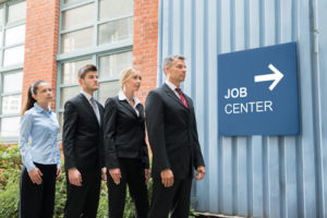 Drei Männer im Anzug und eine Frau im Kostüm vor einem Schild zum Job Center