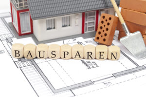 Auf einem Bauplan steht ein Spielzeughaus und Buchstabenwürfel, die das Wort Bausparen bilden