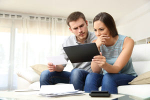 Ein besorgtes Paar auf der couch checkt seine Unterlagen und nutzt einen Tablet Computer