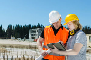 Zwei junge Männer mit Bauhelmen und einem Tablet Computer vor einer Baustelle