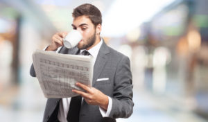 Ein Mann mit Anzug ließt eine Zeitung und trinkt dazu Kaffee