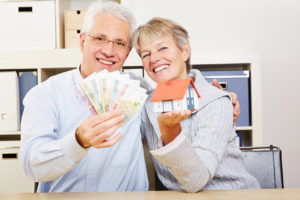 Glückliches älteres Paar hält ein paar Geldscheine und ein Modellhaus vor sich