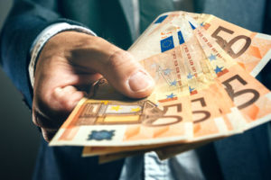 Ein Mann im Anzug streckt ein paar fünfzig Euro Scheine vor