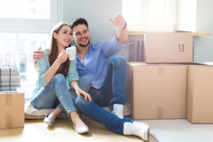 Ein junges Paar sitzt neben Umzugskartons und richten geistig die neue Wohnung ein