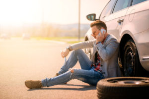 Ein Mann beim Reifenwechseln sitzt neben seinem Auto und telefoniert