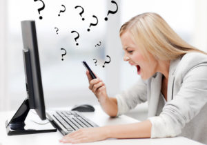 Eine junge Frau sitzt vor ihrem Computer und schreit in ihr Handy