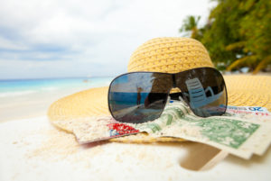 Ein Sommerhut mit Sonnenbrille und einigen Geldscheinen liegt auf dem Sandstrand