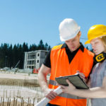Zwei junge Männer stehen auf einer Baustelle und betrachten etwas auf einem Tablet Computer