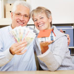 Fröhliches älteres Paar zeigt Geldscheine und ein Modelhaus