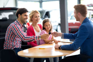 Eine glückliche Familie mit Kind nimmt beim Autohändler den Fahrzeugschlüssel in Empfang