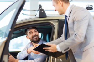 Ein Kunde sitzt im Auto und gibt dem Autohändler die Hand