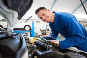 Ein junger Ingenieur mit Tablet Computer beugt sich über einen Automotor