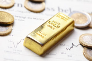 Ein kleiner Goldbarren liegt auf einem Blatt mit Daten und Kurse neben einigen Münzen