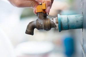 Jemand dreht einen außenliegenden Wasserhahn zu