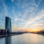 Das Gebäude der EZB vor blauem Himmel und aufgehender Sonne